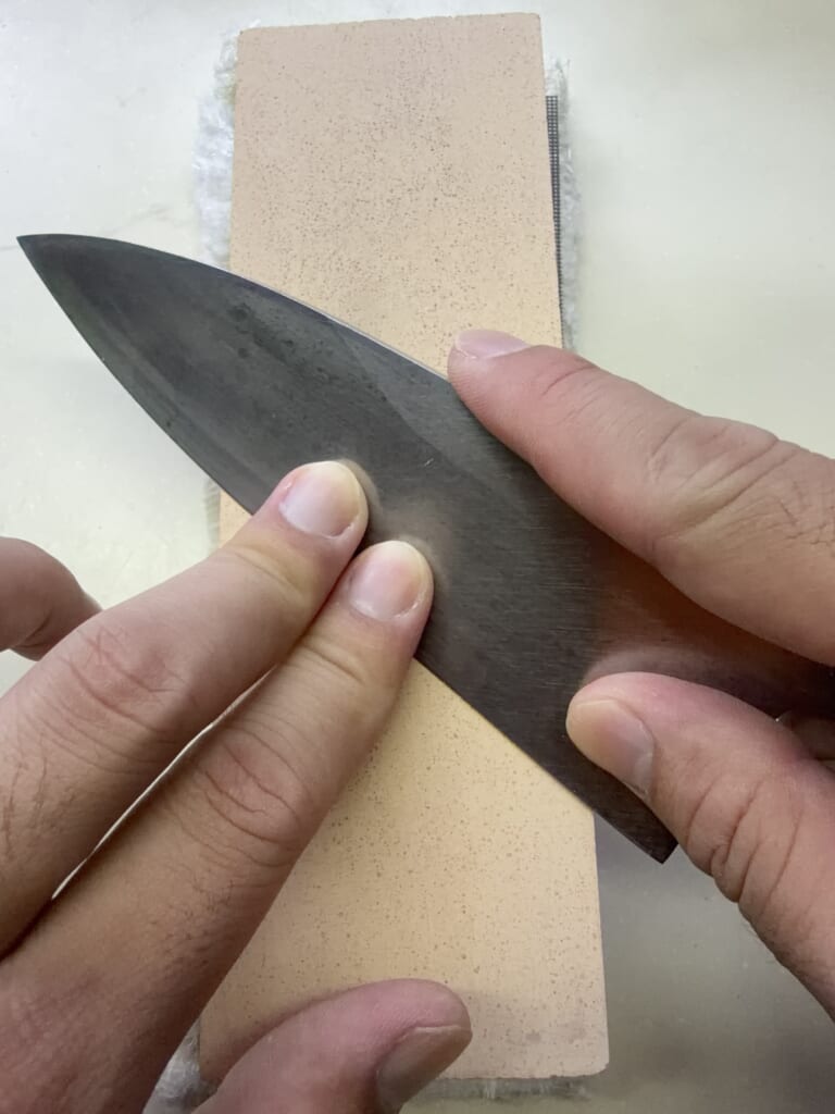 出刃包丁の切刃を砥石に当て、指で押さえながら研いでいる様子
